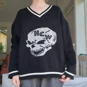 Skull college sweater - Svart stickad college tröja med vit döskalle och text, tror den är från shein. V-ringad med vita ränder vid hals, ärmslut och nederkant. Oversized passform och långa ärmar, perfekt för alternativ stil.