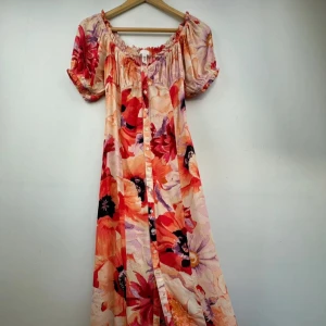 Blommig långklänning i nyskick - Superfin långklänning med stora blommotiv. Klänningen har puffiga korta ärmar, knappar hela vägen framtill och en smockad offshoulder-ringning. Passar en strlk small. Superfin somrig vibe, perfekt till midsommar! 🌸