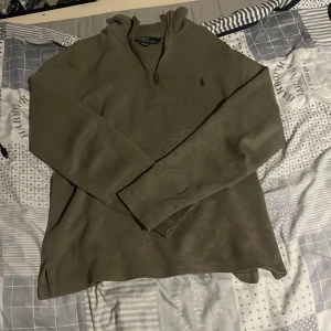 Beige stickad tröja med dragkedja från Polo Ralph Lauren - Säljer en beige stickad tröja från Polo Ralph Lauren med halv dragkedja och liten broderad logga på bröstet. Tröjan har lång ärm och klassisk passform, perfekt för lager-på-lager-stil.