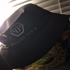 Svart bucket hat från Philipp Plein - Svart bucket hat med Philipp Plein-logga tryckt på sidan. Klassisk form och stilren design, perfekt för att lyfta din outfit med en exklusiv touch.