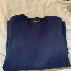 Mörkblå stickad tröja Brand Island - En stilren mörkblå stickad tröja från Brand Island i storlek M. Tröjan har rund halsringning med ribbade detaljer och långa ärmar. Perfekt för lager-på-lager och funkar till både jeans och chinos.