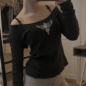 Svart långärmad topp med tryck - Svart långärmad topp med rund halsringning och ett tryck av en bevingad dödskalle framtill. Jätte söt men kommer aldrig till användning + är för lång i armarna på mig :( Köpt i London för ca 300kr, buda gärna !💗