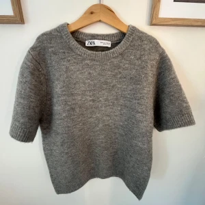 Grå stickad kortärmad tröja Zara - Mysig grå stickad tröja från Zara med korta ärmar och rund hals. Tröjan är från Zara och är i storleken S. Tröjan är endast använd en gång och är därav i ett mycket bra skick. Den är även supermjuk i materialet. 