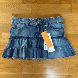 Blå volang jeanskjol från Ginatricot - Supersöt blå jeanskjol från Ginatricot med volanger och råa kanter. Kjolen har klassiska fickor fram och bak, låg midja och coolt sliten look. Perfekt för dig som vill ha en trendig och avslappnad stil. Efterfrågad!! Ny med prislapp kvar!!