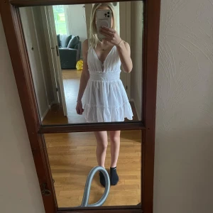 Vit kort sommarklänning med volang - Supersöt vit kort klänning med volanger. v-ringning framtill och öppen rygg. Perfekt för varma dagar, lätt och luftig i bomull. Ger en fräsch och somrig vibe!