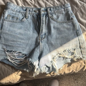 Ljusblå jeansshorts från SHEIN XXS - Snygga ljusblå jeansshorts från SHEIN i storlek XXS. Modellen är högmidjad med fransiga kanter och slitningar framtill för en cool, avslappnad vibe. Klassisk femficksdesign och dragkedja med knapp. Perfekta för varma dagar och festivalhäng.