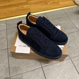 Mörkblå loubs storlek 42 - Snygga mörkblå sneakers från Louboutin i mocka med klassisk röd sula och diskret broderad logga på sidan. Skorna har rund tå, platt sula och snörning. Insidan är fodrad i beige läder för extra komfort. Perfekta för dig som vill sticka ut med stil.