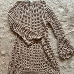 Strandklänning - Beige stickad nätklänning från H&M med lång ärm och lätt utsvängda ärmslut. Klänningen har ett grovmaskigt, virkat mönster och är perfekt att styla över ett linne eller bikini. Storlek S🐚🌊💙