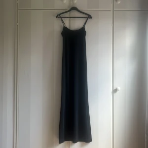Svart långklänning med smala axelband - En stilren svart långklänning med smala axelband och rak passform. Perfekt för dig som gillar minimalistisk stil och vill ha en enkel men snygg klänning till sommaren. Nypris 300, säljer för 150. 