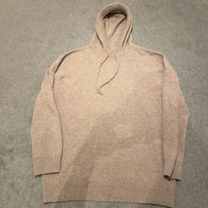 Beige stickad hoodie - Säljer en mysig beige stickad hoodie med ribbade muddar och dragsko i huvan. Perfekt för kyliga dagar och ger en avslappnad stil. Passar bra till jeans eller mjukisbyxor. 50/50 kashmir och merino ull