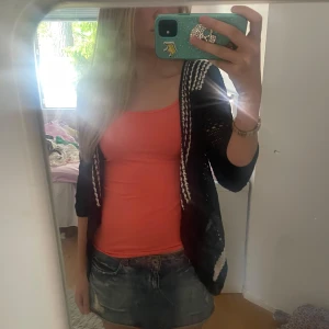 Svart stickad väst från Karen Millen - Säljer en svart stickad väst från Karen Millen med vita och svart detaljer i ett mönster över axlar och rygg. Västen är öppen framtill och har ett luftigt, virkat utseende. Perfekt att slänga över en topp för en cool lager-på-lager-look.