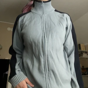 Ljusblå zipup med krage - Ljusblå ziptröja med hög krage och mörkblå ränder längs ärmarna. Tröjan är tillverkad i 100% bomull och har ribbade muddar vid ärmslut och nederkant. Perfekt för en avslappnad och sportig stil. Svaga fläckar på höger ärm, se bild 5.