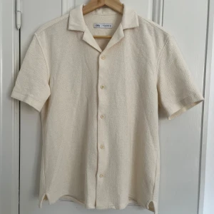 Beige Skjorta från Zara - Säljer denna stilrena kortärmade skjortan från Zara i ett froté-liknande material och en fräsch beige färg, den är perfekt till en fin sommardag. Det är storlek S och den är i nyskick, utan några tecken på användning. Nypris 500kr| Mitt pris 129kr| Tveka inte att höra av dig vid minsta fundering!
