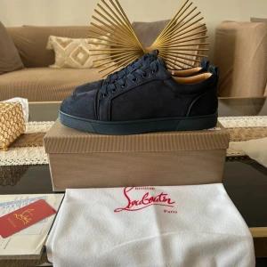 Christian Louboutin skor  - Säljer ett par mörkblå sneakers från Christian Louboutin i mocka med den ikoniska röda sulan. Skorna har rund tå, platt sula och klassisk snörning. Perfekta för dig som vill ha något exklusivt och stilrent.