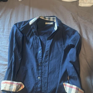 Blå skjorta från Burberry med rutiga detaljer - Snygg blå skjorta från Burberry med klassiska rutiga detaljer på insidan av kragen och ärmsluten. 