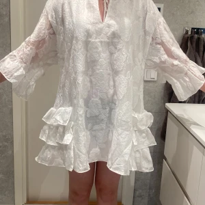 Vit klänning med volanger - Säljer en elegant vit klänning med volanger. Klänningen har en lös passform och är perfekt för student/skolavslutning. Den är tillverkad i ett lätt och luftigt material med ett fint mönster. Strl 38, köpt på Bohoo. Ny, aldrig använd. 