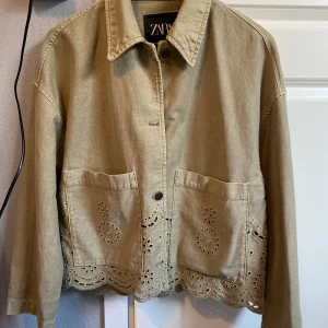 Khaki jacka med broderade detaljer från Zara - Säljer en beige jacka från Zara med stora fickor framtill och broderade blommönster längs nederkanten. Perfekt för dig som gillar unika detaljer och avslappnad stil.