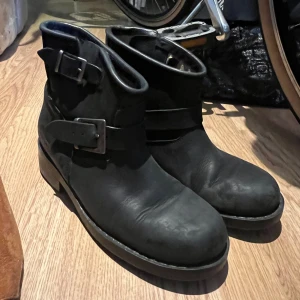 Svarta Johnny Bulls med spännen - Säljer ett par svarta Johnny Bulls boots med två dekorativa spännen och rund tå. Skorna har en robust platt sula och är perfekta både i sommar och vinter 💕 