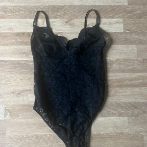 Svart spetsbody från Stay - Säljer en svart body i spets från Stay. Bodyn har tunna axelband och är helt täckt av blommig spets, vilket ger en elegant och feminin look. Perfekt att styla under en kavaj eller till jeans.