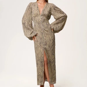 Zebramönstrad adoore klänning  - Säljer en långklänning med zebramönster från adoore. Klänningen har djup v-ringning, långa puffärmar och knappar hela vägen framtill samt en slits. Skriv gärna vid frågor 