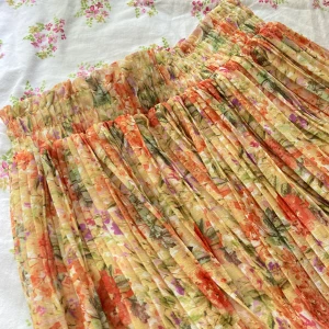 Plisserad blommig kjol i pastellfärger -  plisserad kjol med blommigt mönster. Kjolen har resår i midjan och är fodrad med ett vitt innerfoder. 