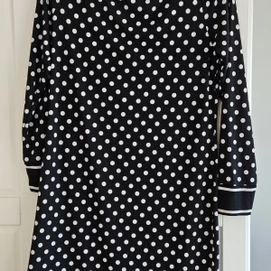 Svart prickig klänning från Michael Kors - Säljer en svart klänning med vita prickar från Michael Kors. Klänningen har lång ärm och en rak, avslappnad passform. Perfekt för dig som gillar klassiska mönster och stilren design. Stretch skrynklar inte. M/L