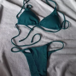 Grön ribbad bikini med knyt - Säljer en grön bikini med ribbad struktur. Toppen har trekantsform och knytband både i ryggen och nacken. Underdelen har högt skuren modell med knyt i sidorna. Perfekt för stranden eller poolen!