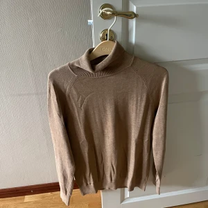 Beige polotröja från Bläck - Snygg beige polotröja från Bläck med klassisk hög krage och långa ärmar. Tröjan är tunnstickad och har en mjuk känsla, perfekt för lager-på-lager. Passar dig som gillar en stilren och enkel look.