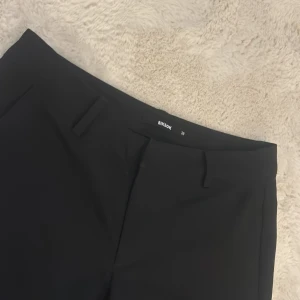 Svarta kostymbyxor från Bik Bok - Stilrena svarta kostymbyxor från Bik Bok i klassisk rak modell. Byxorna har hällor för bälte, diskreta fickor och är tillverkade i ett mjukt material som känns bekvämt hela dagen. Perfekta för en clean och snygg look. Medellåg midjade. 