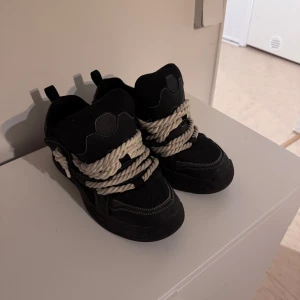 Svarta sneakers med grova vita snören - Säljer ett par svarta sneakers med riktigt breda och grova vita snören. Skorna har en chunky design och rund tå, med kontrasterande sömmar och detaljer. Perfekta för dig som vill sticka ut med din stil. Storlek 43