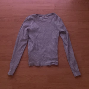 Grå långärmad tröja från KappAhl - En enkel och stilren grå långärmad tröja från KappAhl. Tröjan har rund halsringning och är tillverkad i ett mjukt material som passar perfekt till vardags. Snygg att matcha med jeans eller kjol.