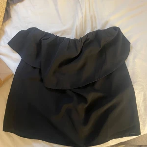 Svart bandeau volangtopp - Supersnygg svart bandeau topp med bred volang upptill.  Den har en enkel men trendig look som passar perfekt till sommaren. Materialet känns mjukt och följsamt, och volangen ger en extra touch till outfiten.