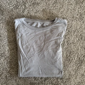 Ljusgrå t-shirt från Replay - Snygg ljusgrå t-shirt från Replay med liten broderad R-logga på bröstet. Klassisk rund halsringning och korta ärmar. Tillverkad i mjuk bomull som känns skön mot huden. Perfekt för en clean och enkel stil.