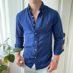 Mörkblå Ralph Lauren skjorta slim fit - Inga defekter förutom en väldigt liten liten vit plupp som är bredvid loggan. Kan gärna skicka bild men kan vara svårt att få bild på det… modellen är 180,75 kg och bär S slim fit. Kom med frågor!
