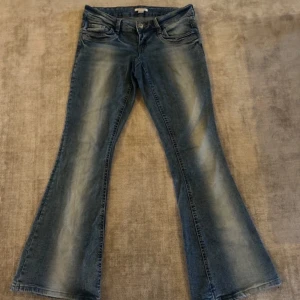 low bootcut jeans med vita slitningar längs benen.  - Snygga low waist blå jeans med bootcut-modell och coola slitningar längs benen. Jeansen har klassisk femficksdesign och en lätt utsvängd passform nertill. Köpta från Gina Young 14+ i storleken M. Köpta för 350kr och använda några gånger. Pris kan diskuteras i dm. 