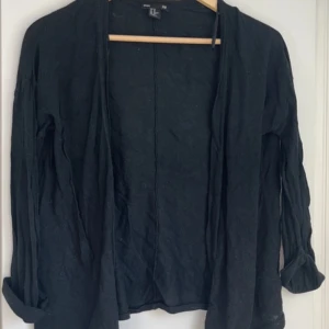 Svart cardigan jacka från H&M XS - Svart cardigan jacka från H&M i storlek XS. Jackan är öppen framtill, har långa ärmar och är tillverkad i en mjuk blandning av viskos och bomull. Perfekt för lager-på-lager och enkel att matcha med allt.