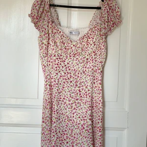 Blommig sommarklänning från Zara - Supersöt blommig klänning från Zara med kort ärm och smockad överdel. Klänningen är vit med små rosa blommor och har en romantisk vibe. Perfekt för varma dagar och har en luftig, lätt passform. Köparen betalar frakten 