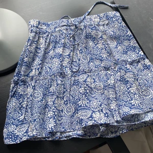 Blåvit blommig kjol från Zara - Supersöt kort kjol från Zara i blått och vitt med blommigt mönster. Kjolen har volangdetalj och knytband i midjan❤️