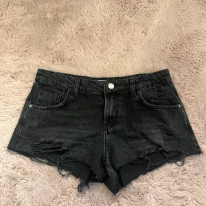 Jeansshorts  - Snygga svarta jeansshorts från Zara med slitna detaljer och råa kanter. Klassisk femficksmodell med knapp och dragkedja framtill. I storlek 36 och jag säljer de för att de inte kommer till användning!!❤️