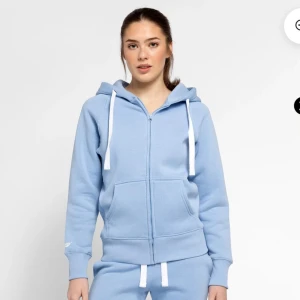 Ljusblå zipkofta från russemerch  - Ljusblå hoodie från russemerch med vit snörning i huvan och dragkedja framtill. Tröjan har ribbade muddar, två fickor och en relaxed passform.  Storlek xxs. Använd ish 5 gånger 