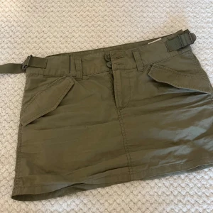 Grön cardigan kjol  - Snygg olivgrön kortkjol med två stora fickor fram och två bak. Kjolen har bältdetalj i midjan och stängs med dubbla knappar och dragkedja. Perfekt för en avslappnad och cool stil, passar till sneakers eller boots. Den justeras beroende på hur din kroppsform är så storleken är inte ett problem jag själv är s och den passar perfekt när jag justerar🤍 