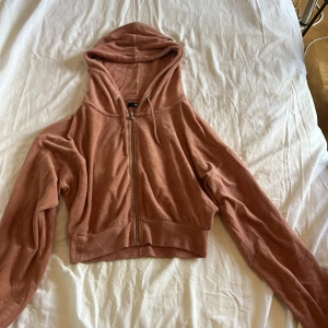 Rostbrun croppad hoodie från Bik Bok - Säljer en croppad hoodie från Bik Bok i en snygg rostbrun färg. Tröjan har dragkedja framtill, huva med snörning och långa ärmar. Materialet är mjukt och känns som bomullsfrotté, perfekt för chill dagar.