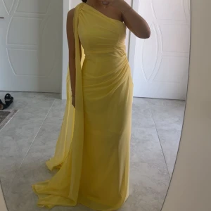 Gul långklänning med oneshoulder - Snygg gul långklänning med oneshoulder och draperad design. Klänningen har ett elegant fall och en lång släp på ena axeln som ger en extra touch. Perfekt för dig som vill sticka ut med en färgstark och stilren look. St M men passar även nån som har S💛