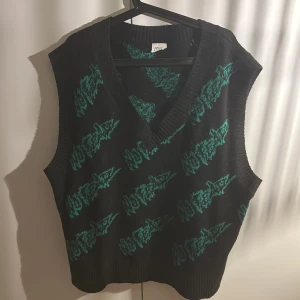 Svart stickad väst med coolt tryck  - Svart stickad väst med grönt grafiskt mönster, djup v-ringning och oversized fit. 