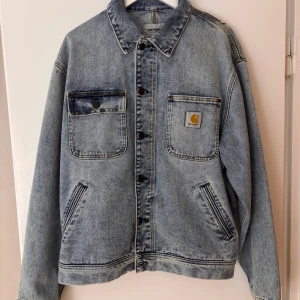 Oversized jeansjacka från Carhartt WIP  - Säljer en oversized ljusblå jeansjacka från Carhartt med klassisk krage, två stora bröstfickor och tydliga sömmar. Jackan har knappar framtill och Carhartt-logga på ena fickan. Perfekt för dig som gillar streetwear och avslappnad stil.
