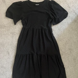 Svart kortklänning från JDY - Supersöt svart kortklänning från JDY med broderade hål och puffiga korta ärmar. Klänningen har rund halsringning och ett luftigt fall, perfekt för dig som gillar en chill men ändå stylish look.