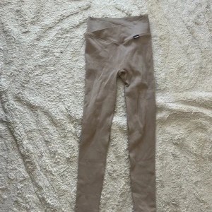 Beige ribbade leggings från Stronger XS - Supersnygga beige leggings från Stronger i ribbat material. De har hög midja med omlott-detalj och sitter tight och bekvämt. Perfekta för träning eller chill. Storlek XS.
