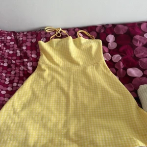 Gul rutig sommarklänning med knytband - Supersöt gul och vit rutig klänning med smala axelband som knyts på axlarna. Klänningen är kort och har en lätt utställd passform, perfekt för varma dagar. Tunt och luftigt material som känns fräscht och somrigt.