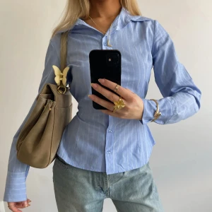 Figurnära skjorta - Smickrande skjorta från design by si som man knyter i ryggen. I storlek M/L men sitter som S. Oanvänd utan prislapp.