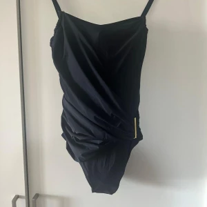 Svart baddräkt från Calvin Klein XS - Snygg svart baddräkt från Calvin Klein med justerbara axelband och guldfärgad detalj i sidan. Perfekt för stranden eller poolen, klassisk och stilren design. Nypris 1000kr